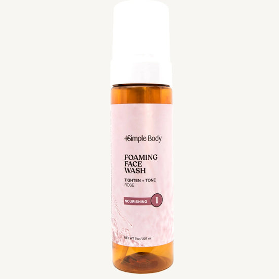 An amber colored pump bottle of Simple Body Foaming Face Wash with pink rose floral water visible inside.