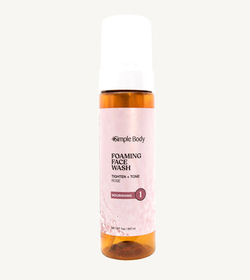 An amber colored pump bottle of Simple Body Foaming Face Wash with pink rose floral water visible inside.