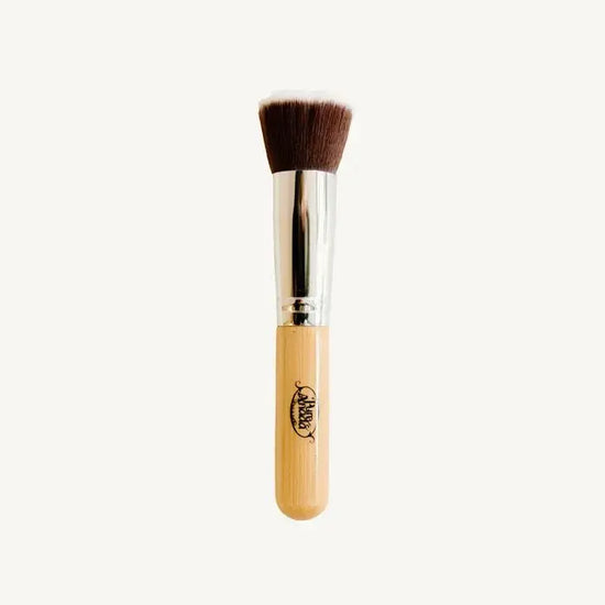 A photo of Pure Anada's Flat Top Makeup Brush which is brown and fades to white on the bristles with a wooden handle on a tan background.