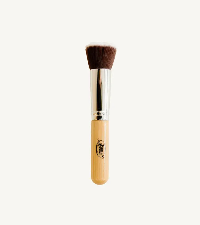 A photo of Pure Anada's Flat Top Makeup Brush which is brown and fades to white on the bristles with a wooden handle on a tan background.