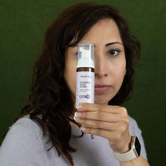 A woman looking straight ahead holding a travel size Simple Body Foaming Face Wash in lavender.