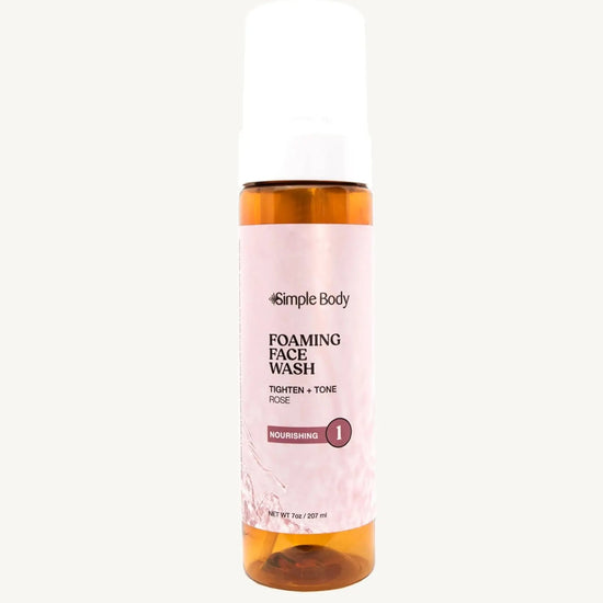 An amber colored pump bottle of Simple Body Foaming Face Wash with pink rose floral water visible inside.