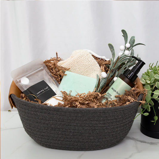 A photo of a gift basket featuring bath salt, a handmade Rosemary Mint soap, a cotton soap sack, Rosemary Mint body lotion all in a beautiful gray rope basket.