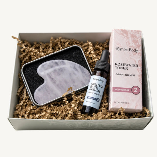Simple Body Gua Sha gift set including a gua sha tool, Nightly Face Serum, and a Rosewater Toner in a box with crinkled paper