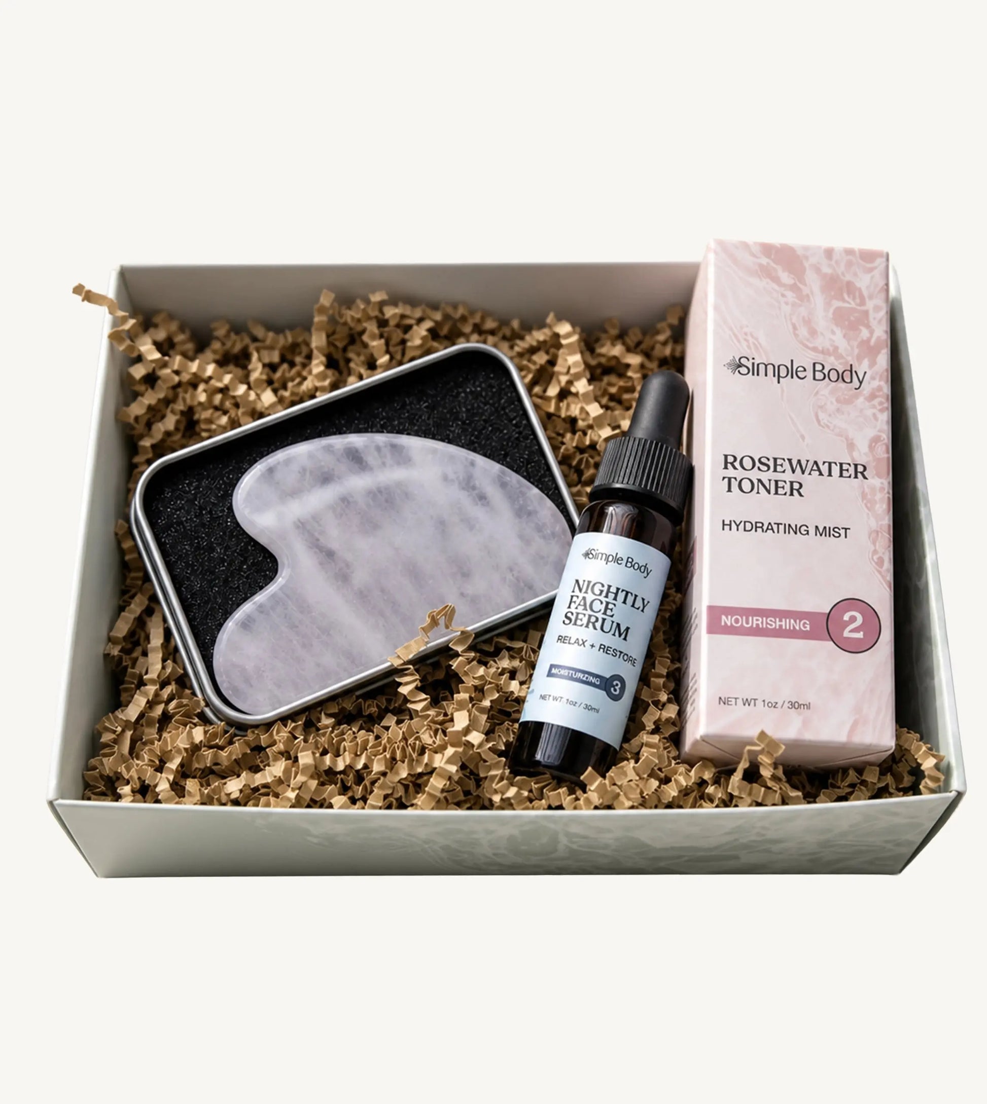 Simple Body Gua Sha gift set including a gua sha tool, Nightly Face Serum, and a Rosewater Toner in a box with crinkled paper