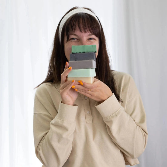 Person holding a stack of colorful Simple Body handmade soap bars against a white background