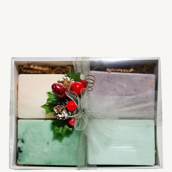 Set of Simple Body handmade soaps including Himalayan Magic Soap, Breathe Better Eucalyptus soap, Lemongrass soap, and Rosemary Mint Soap with decorative elements in a box on a white background