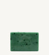 A handmade bar of soap with a green color and an embossed design on it, placed against a tan background.