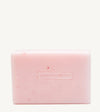 A handmade bar of soap with a pink color and an embossed Simple Body design on it, placed against a tan background.