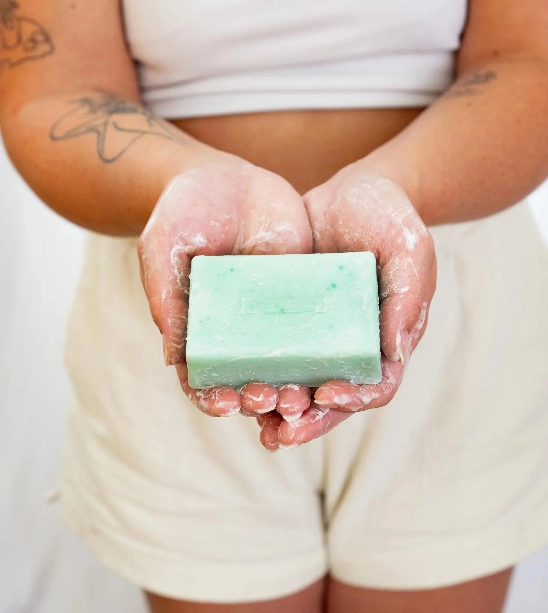 Person holding a bar of Simple Body Rosemary Mint green soap with soapy hands against a neutral background