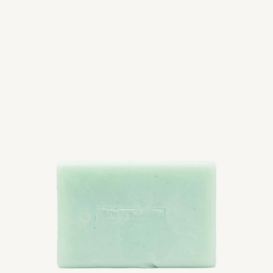 A handmade bar of soap with a mint color and an embossed design on it, placed against a tan background.