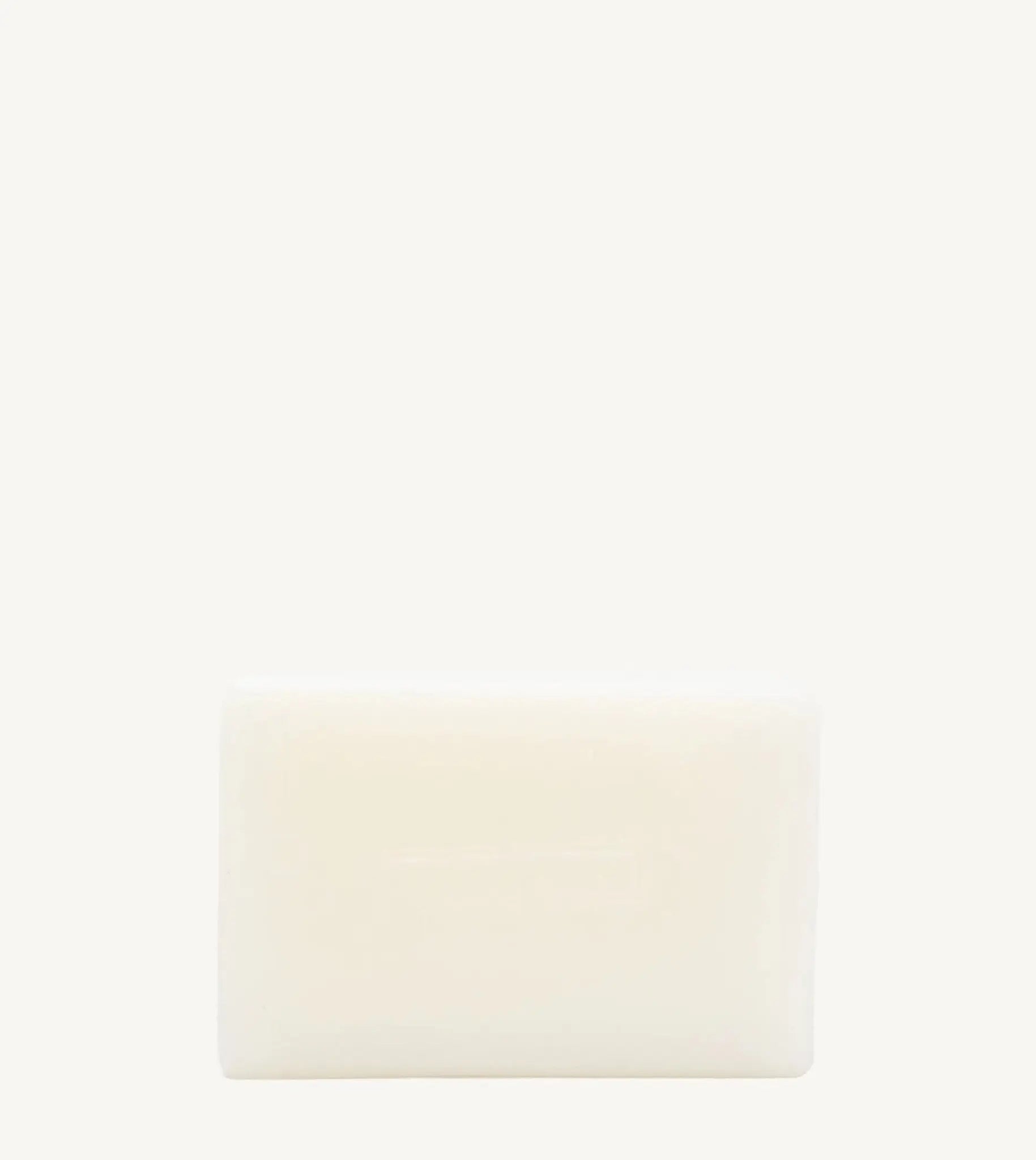 A handmade bar of soap with an off-white color and an embossed design on it, placed against a tan background.