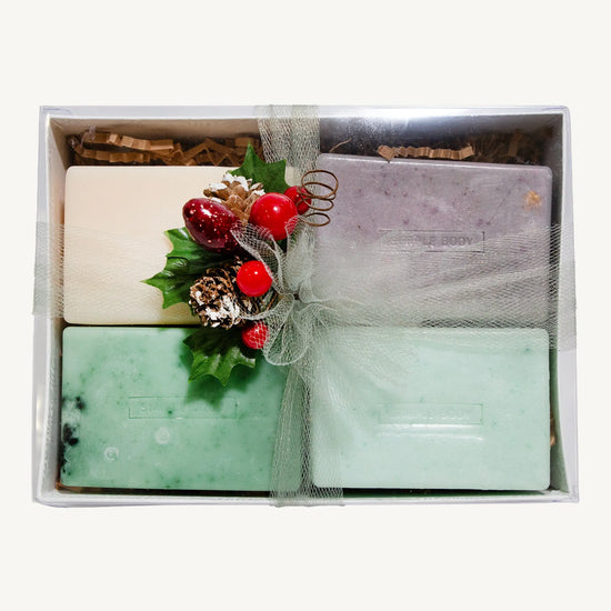 Set of Simple Body handmade soaps including Himalayan Magic Soap, Breathe Better Eucalyptus soap, Lemongrass soap, and Rosemary Mint Soap with decorative elements in a box on a white background