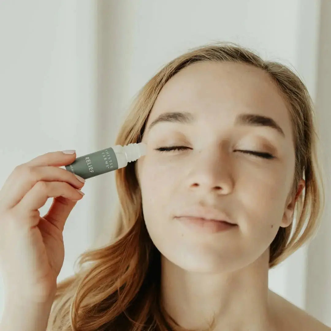 Woman applying an essential oil roller to her face with a neutral background