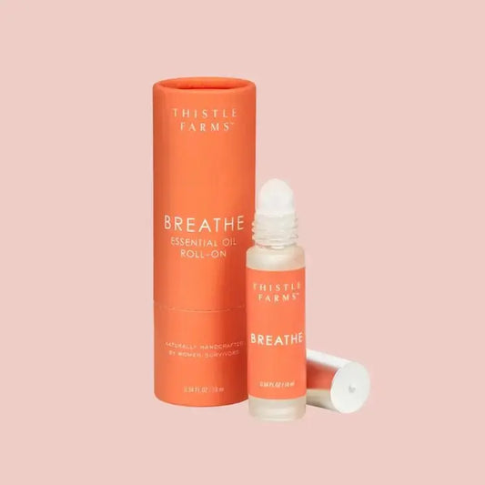 Thistle Farms Breathe essential oil roll-on bottle and packaging on a pink background