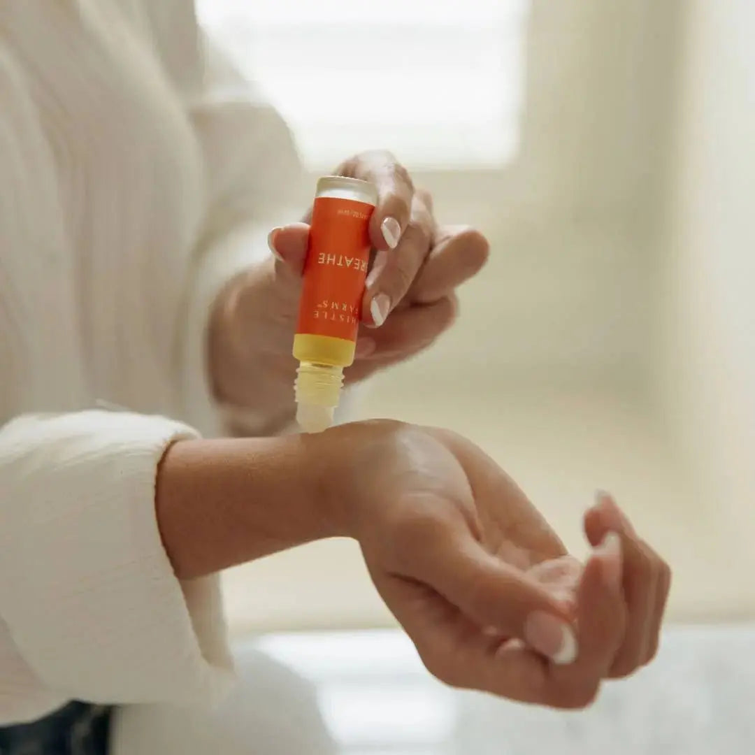 Person applying an essential oil product to their wrist with a blurred background 