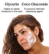 A young woman looks to the side with long dark hair and Simple Body Foaming Face Wash applied to her cheek on a white background with Glycerin and Coco Glucoside called out as key ingredients.