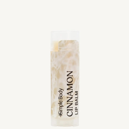 An oval lip balm tube with a label that reads 'Cinnamon Lip Balm'. The packaging is clear, revealing the off-white product inside.
