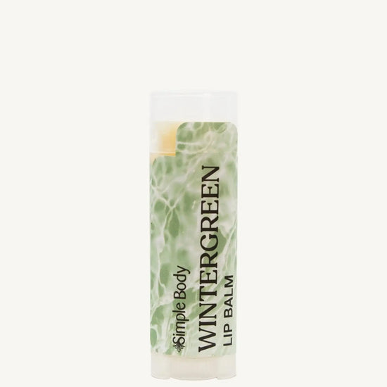 An oval tube of Simple Body Wintergreen Lip Balm with a green and white label, indicating it is nourishing lip care with a minty scent.