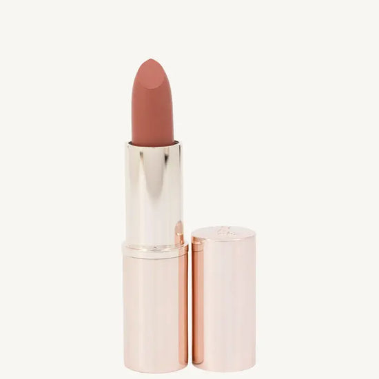 A photo of Pure Anada's Carefree Matte Lipstick in a rose gold tube and a warm orange - rust color on a tan background.