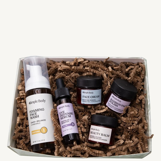 A Simple Body Mini Facial Kit that includes a Chamomile Foaming Face Wash Calm and Balance, Eye Defense Serum to Revitalize and Brighten, Face Cream for Moisture Renewal with Green Tea, Bamboo Face Polish Exfoliating Cleansing Scrub, and Beauty Balm Vitamin C Super Boosting Moisturizer with kraft shred on a white background.