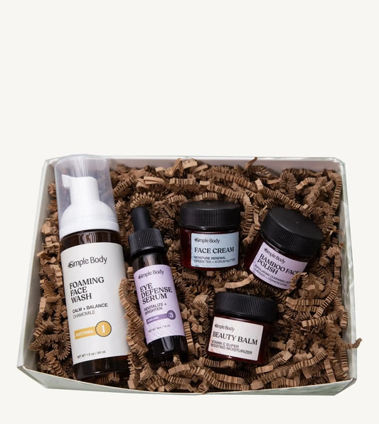 A Simple Body Mini Facial Kit that includes a Chamomile Foaming Face Wash Calm and Balance, Eye Defense Serum to Revitalize and Brighten, Face Cream for Moisture Renewal with Green Tea, Bamboo Face Polish Exfoliating Cleansing Scrub, and Beauty Balm Vitamin C Super Boosting Moisturizer with kraft shred on a white background.