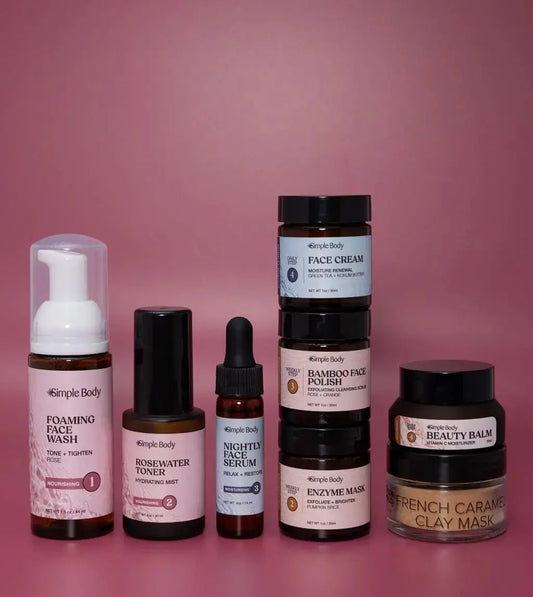 A Mini Starter Skincare kit for normal to dry skin including a Foaming Face Wash, Rosewater Toner, Nightly Face Serum, Face Cream, Bamboo Face Polish, Enzyme Mask, Beauty Balm, and Clay Mask on a rosey pink background.