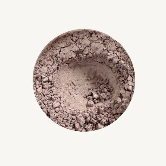 Close-up of Pure Anada's Mountain Haze loose eye shadow in a beige shimmery powder on a light tan background