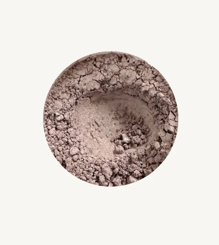 Close-up of Pure Anada's Mountain Haze loose eye shadow in a beige shimmery powder on a light tan background