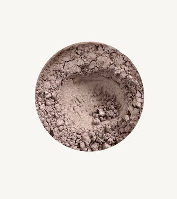 Close-up of Pure Anada's Mountain Haze loose eye shadow in a beige shimmery powder on a light tan background