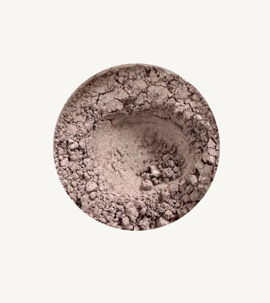 Close-up of Pure Anada's Mountain Haze loose eye shadow in a beige shimmery powder on a light tan background