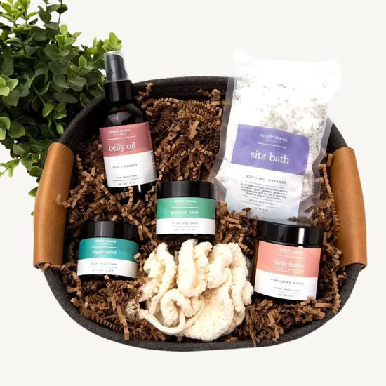 A gift basket containing various skincare products including a sitz bath packet, belly oil, belly butter, perineal and nipple balms, and a cotton pouf, all arranged in a reusable cotton rope basket.