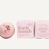 A pink bath bomb by Ginger June Bath Co with dried flower petals sits next to two pink product boxes labeled 'bath bomb' and 'pillow talk' on a clean white background.