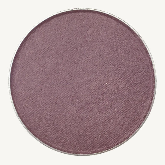 A photo of Pure Anada's Pressed Eye Color in Grape which is a deep purple color on a tan background.
