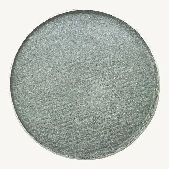 A photo of Pure Anada's Pressed Eye Color in Sterling which is a bluish green shimmery color on a tan background.