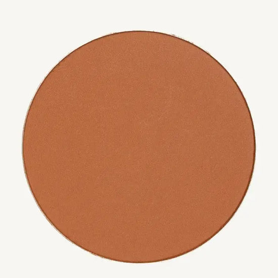 A photo of Pure Anada's Global Pressed Foundation powder which is a cinnamon brown orange color on a tan background.