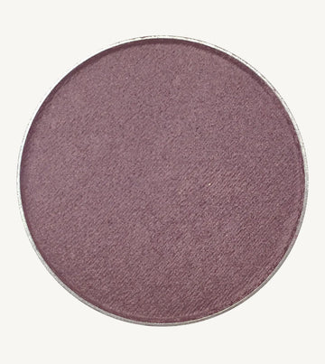A photo of Pure Anada's Pressed Eye Color in Grape which is a deep purple color on a tan background.