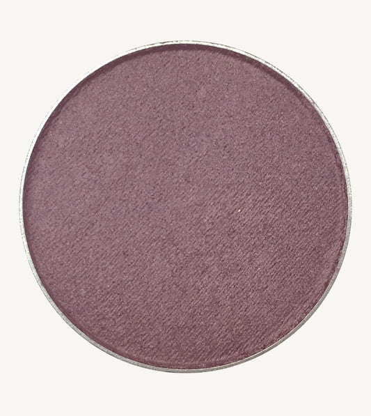 A photo of Pure Anada's Pressed Eye Color in Grape which is a deep purple color on a tan background.