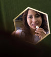 Woman applying a Simple Body Cinnamon lip balm in front of a hexagonal mirror with a green wall background