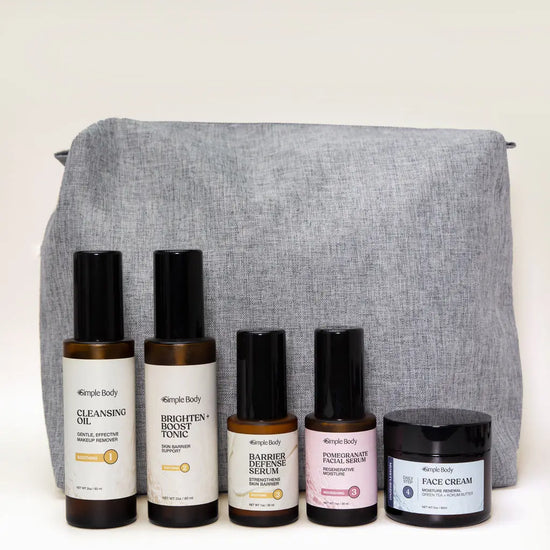 A Skincare Kit designed for sensitive skin including a Cleansing Oil, Brighten and Boost Tonic, Barrier Defense Serum, Pomegranate Facial Serum, Face Cream with a gray carrying case on a white background