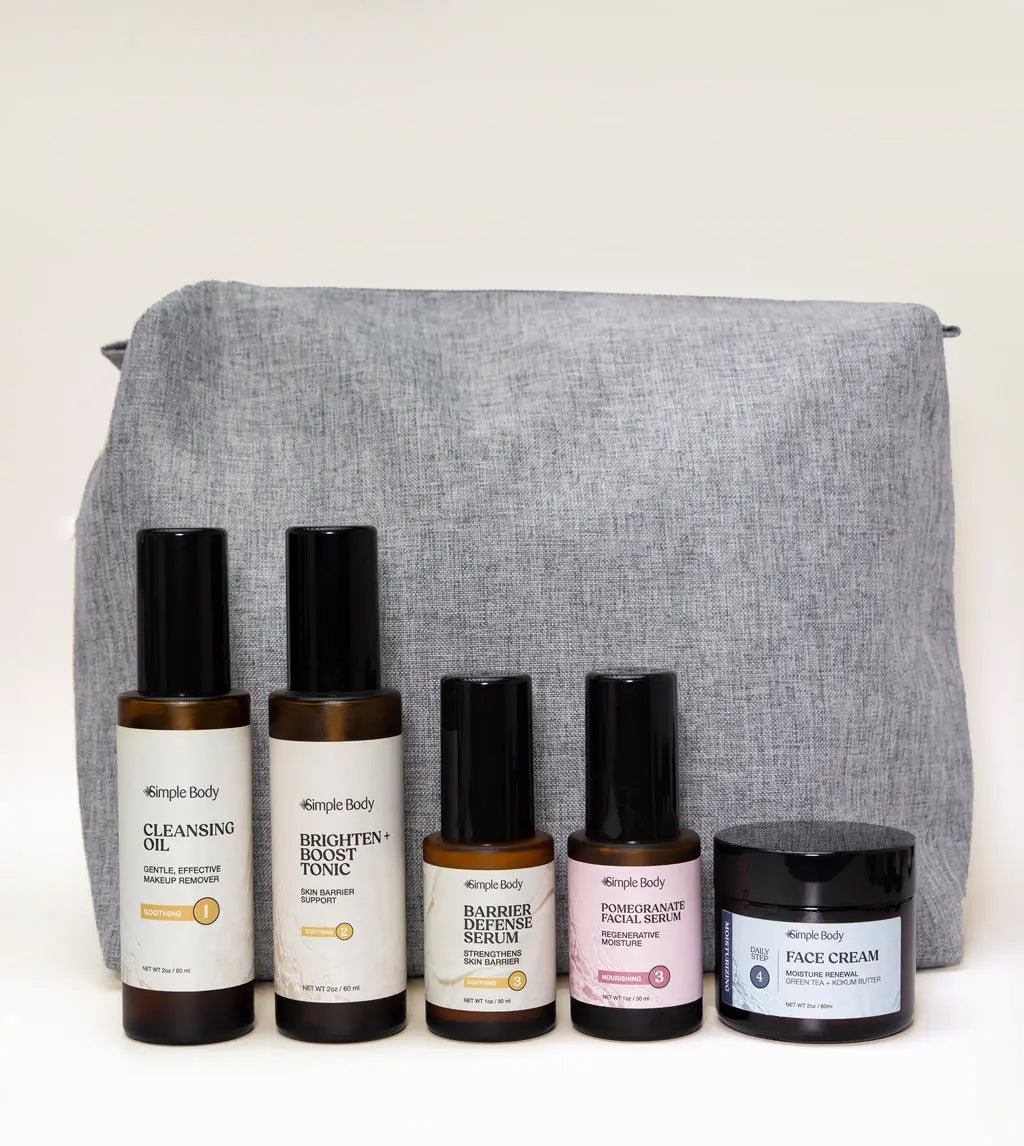 A Skincare Kit designed for sensitive skin including a Cleansing Oil, Brighten and Boost Tonic, Barrier Defense Serum, Pomegranate Facial Serum, Face Cream with a gray carrying case on a white background