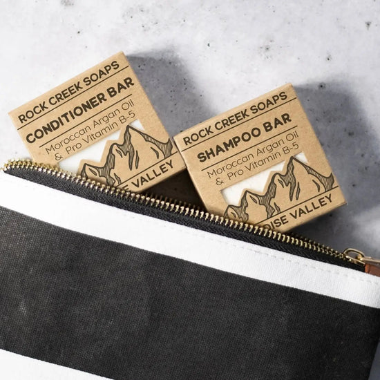 Two shampoo bars from Rock Creek Soaps on a gray surface with a black pouch.