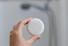 Hand holding a white round object against a blurred background
