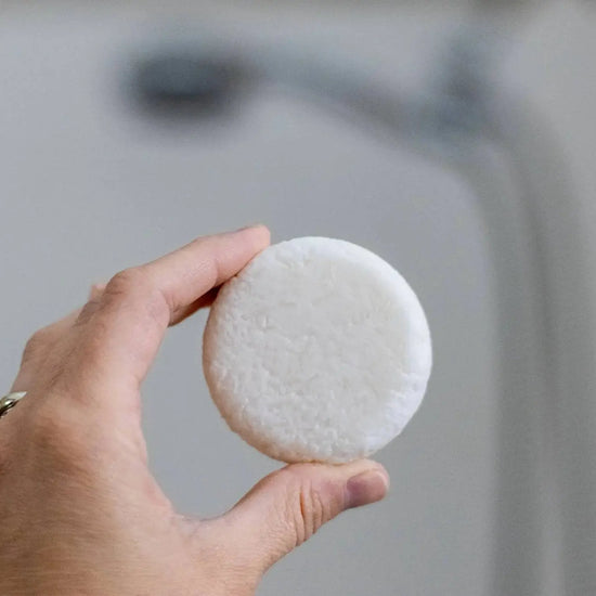 Hand holding a white shampoo bar against a blurred background