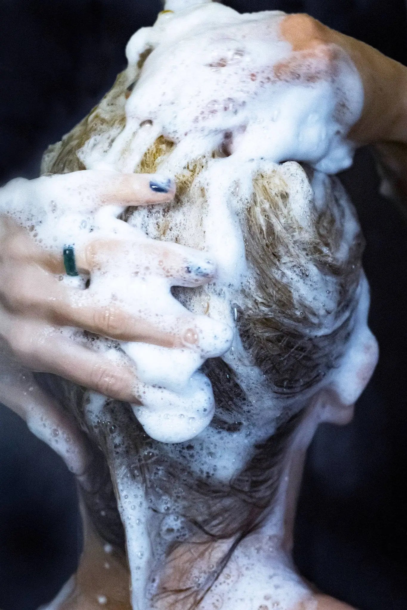 Hand scrubbing hair with a shampoo bar and soap suds against a dark background