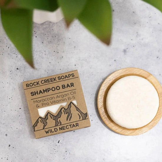 Rock Creek Soaps shampoo bar with packaging on a textured surface with green leaves.
