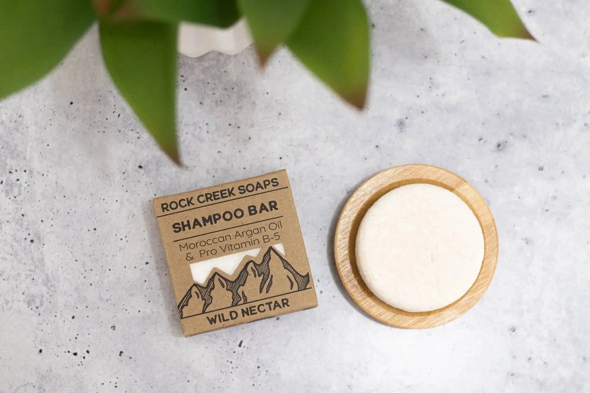 Rock Creek Soaps shampoo bar with packaging on a textured surface with green leaves.