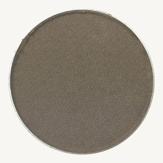 A photo of Pure Anada's Pressed Eye Color in Smoke (Matte) which is a warm brown / gray color on a tan background.