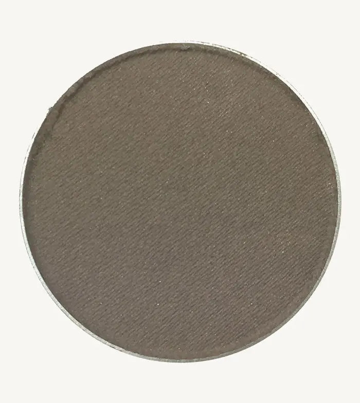 A photo of Pure Anada's Pressed Eye Color in Smoke (Matte) which is a warm brown / gray color on a tan background.