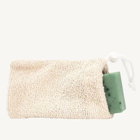 A natural cotton soap saver bag with a green soap bar inside, tied with a white string.